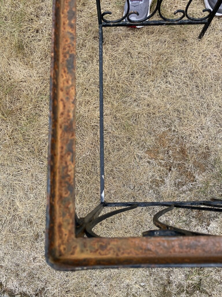 Portion of rusted wrought iron table shown in yard