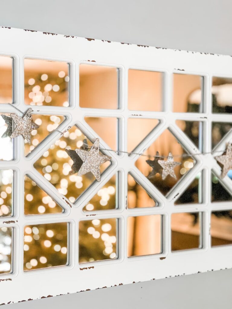 A rustic window with a garland of stars and a Christmas tree in the background