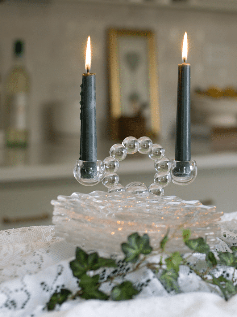 A candlewick candlestick holding two blue/green candles with four crystal dessert dishes in front of the candlestick