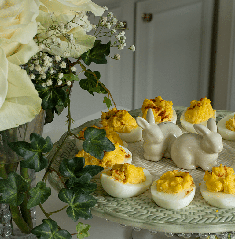 Deviled eggs on a deviled egg plate with bunny salt and pepper shakers in the middle and roses on the side