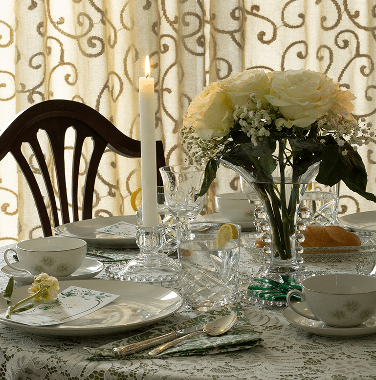 An elegant tablescape with a green and white theme featuring 1960s plates with a single flower, candlewick crystal from the 1960s and a centerpiece of white roses in a candlewick vase.