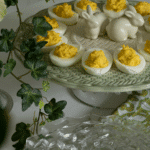 Deviled eggs on a deviled egg dish surrounded by ivy and serving dishes