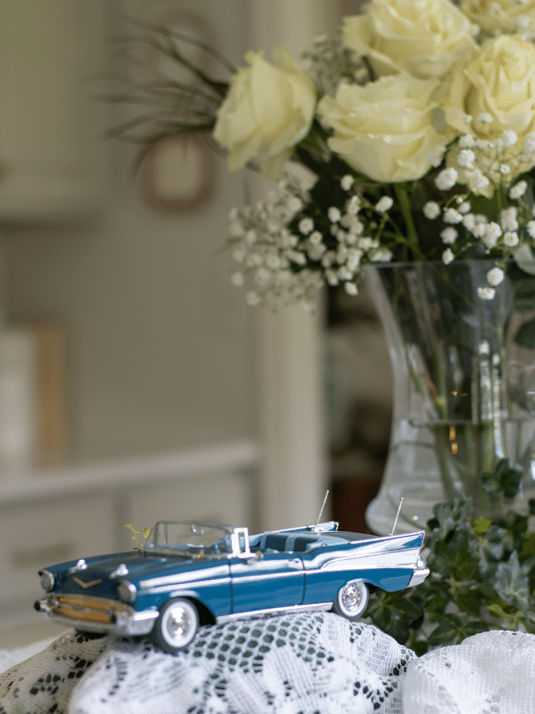 A 1958 blue Chevy convertible mint model car on a lace platform with a bouquet of white roses in the background