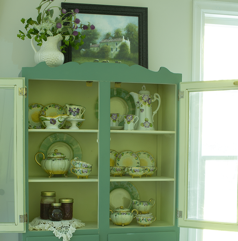 Vintage kitchen cabinet painted green and filled with vintage tea set