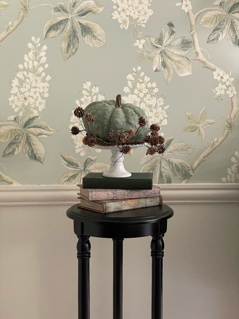 A green pumpkin on a cake stand and perched on books.