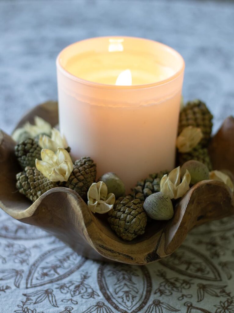 A candle in a wooden bowl surrounded by acorns and chestnuts.