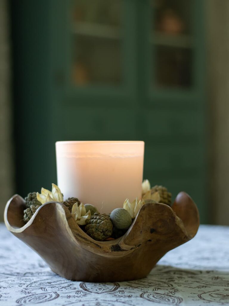 An example of a candle in a wooden bowl surrounded by acorns and chestnuts.