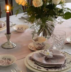 A heart shaped napkin on purple transferware china with white roses in the background