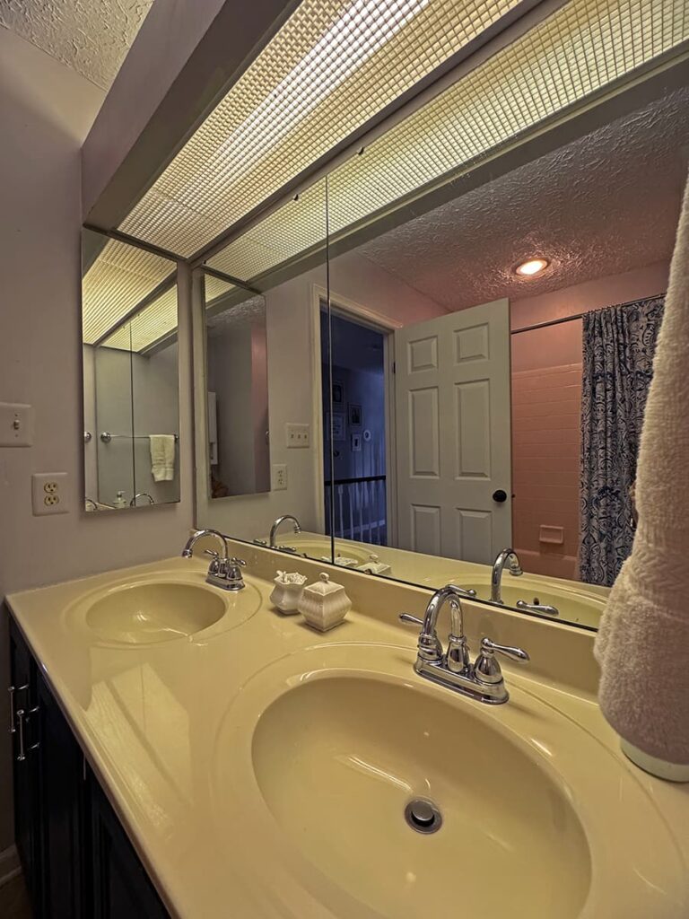 The before of a guest bathroom showing construction grade mirrors and an outdated medicine cabinet