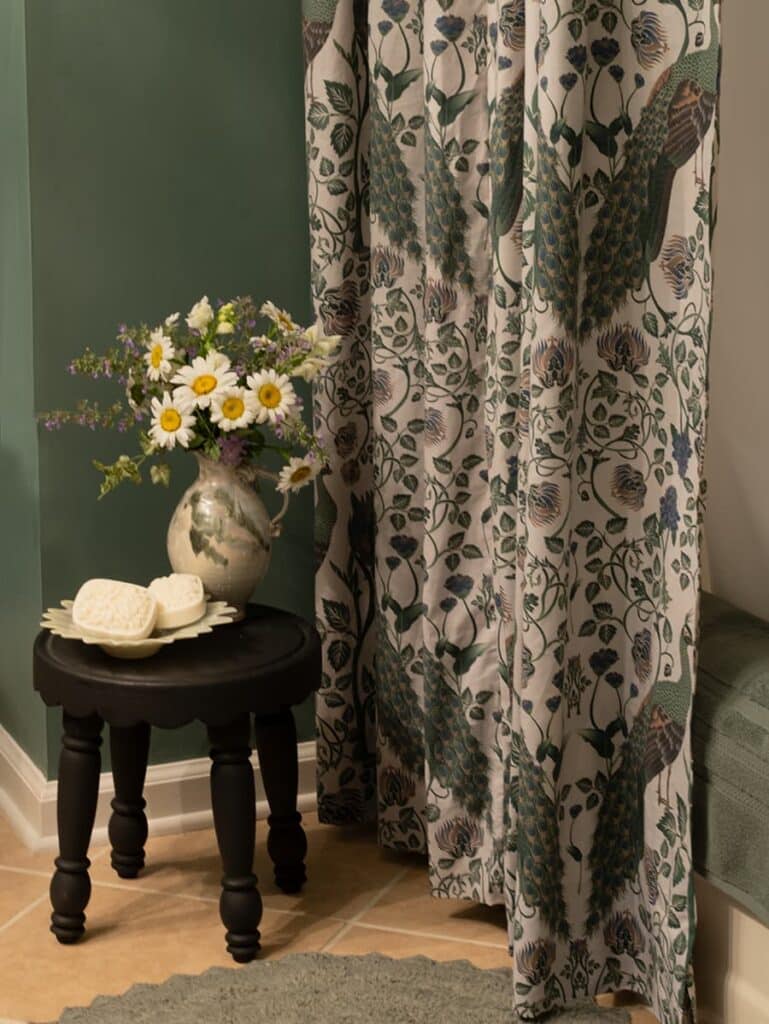 A shower curtain in front of a stool with decorative soaps and a vase of daisies