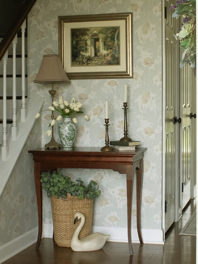 A wallpapered foyer featuring a table that is decorate.
