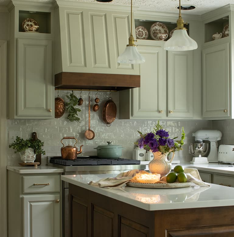 An English country kitchen with a mix of paint and wood tones featuring a brass pot rail