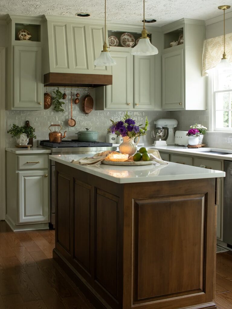 An English country kitchen with perimeter cabinets painted Sherwin Williams Vale mist and a medium brown wood tone island