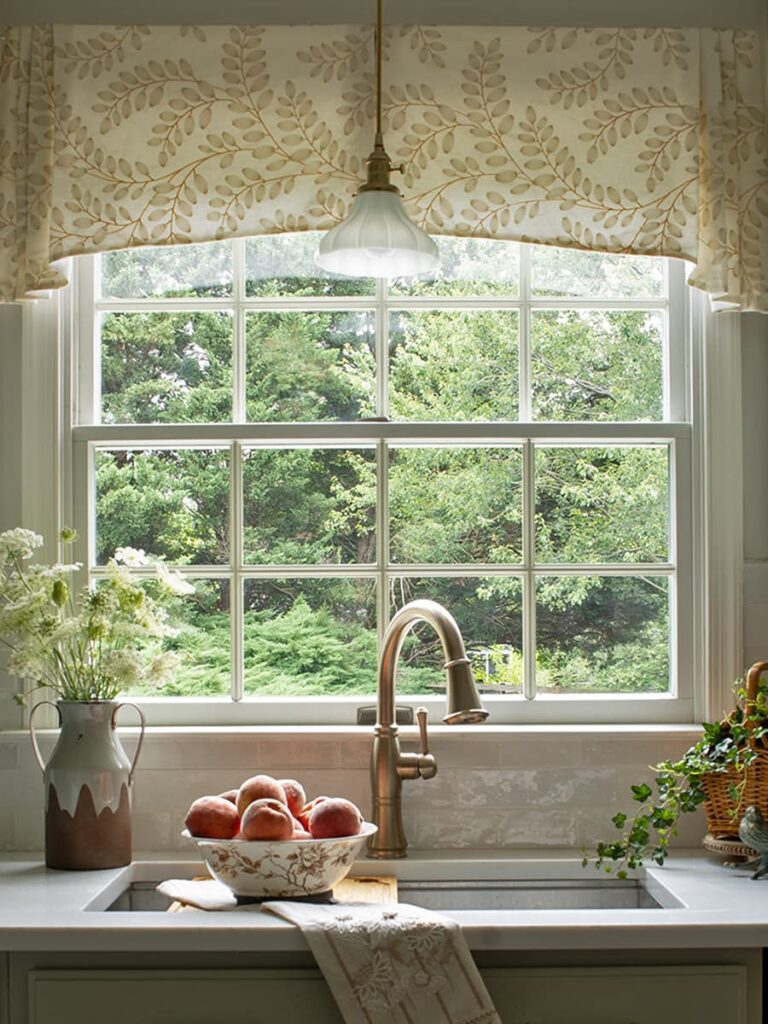 A window above a work station sink and a brass faucet in an English country style kitchen
