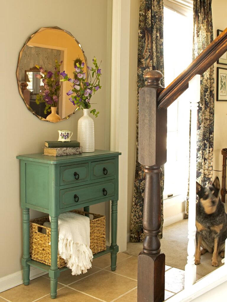 A green table shown in a foyer at the bottom of the stairs